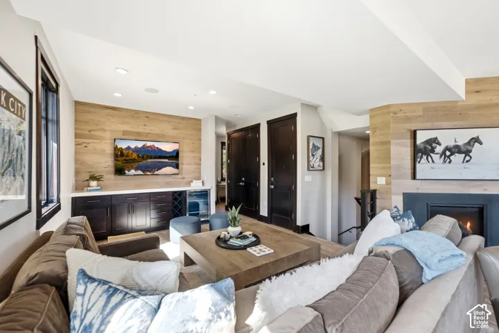 Living area featuring horizontal wood-plank accent walls, built-in dark wood cabinetry with an integrated beverage refrigerator, a recessed fireplace with a dark surround, and dark wood doors
