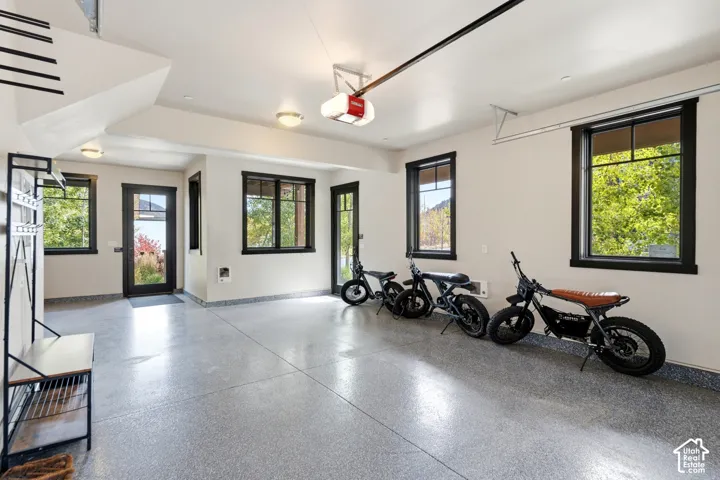 Finished garage space featuring epoxy-coated flooring, multiple windows with black trim, flush-mount ceiling lighting, and dedicated access doors