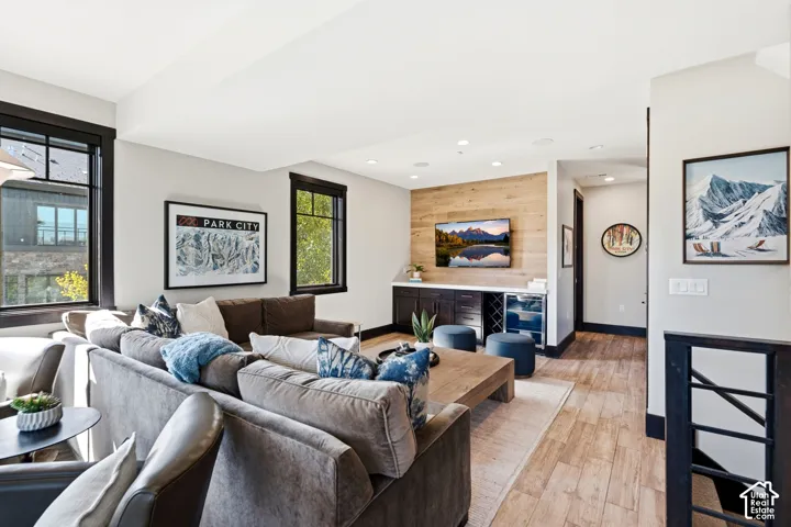 Wood-finish flooring, wood-paneled accent wall, dark built-in cabinetry with integrated wine refrigeration, and oversized windows with black trim