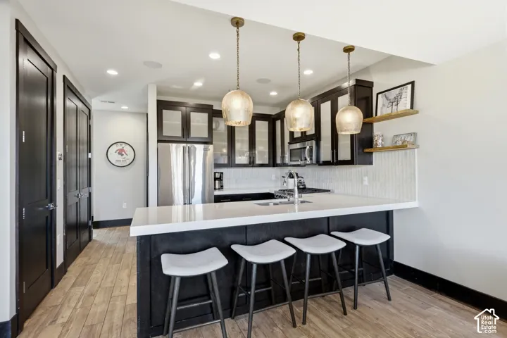 Kitchen featuring dark-stained cabinetry with glass inserts, quartz countertops, an undermount sink, three pendant lights, and wood-finish flooring