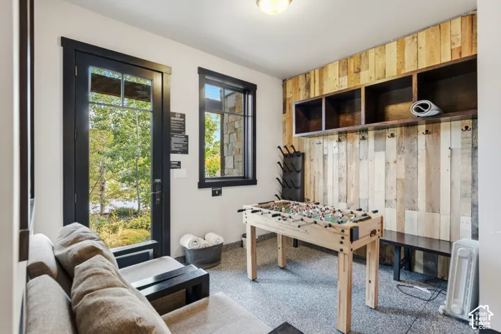Multi-purpose room featuring wood-paneled wall accents, built-in open shelving with integrated coat hooks, epoxy flooring, and a glass-paned exterior door
