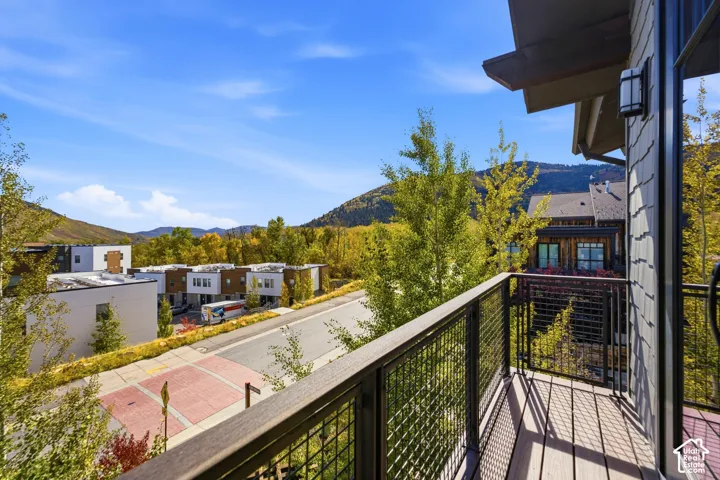 Covered exterior balcony with metal grid railing and wood-toned flooring, featuring mountain terrain and mature landscape surroundings