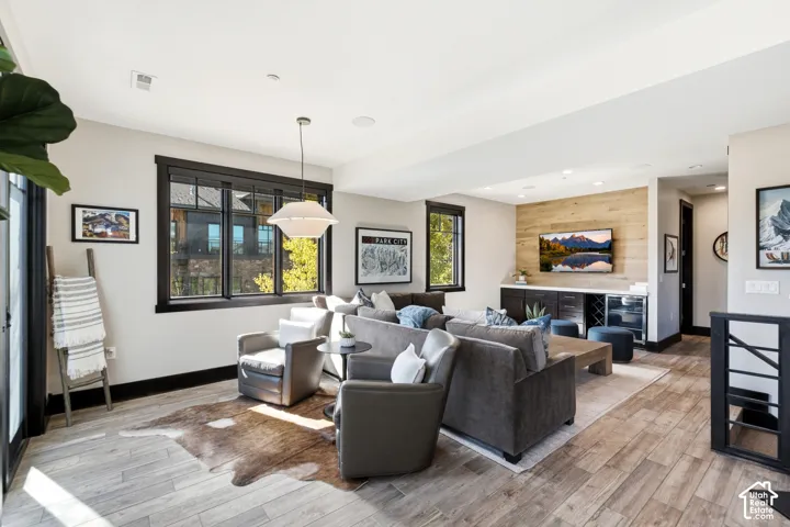 Wood-finish flooring, dark-trimmed windows, recessed lighting, and a built-in media console with wood-paneled accent wall and integrated beverage refrigerator