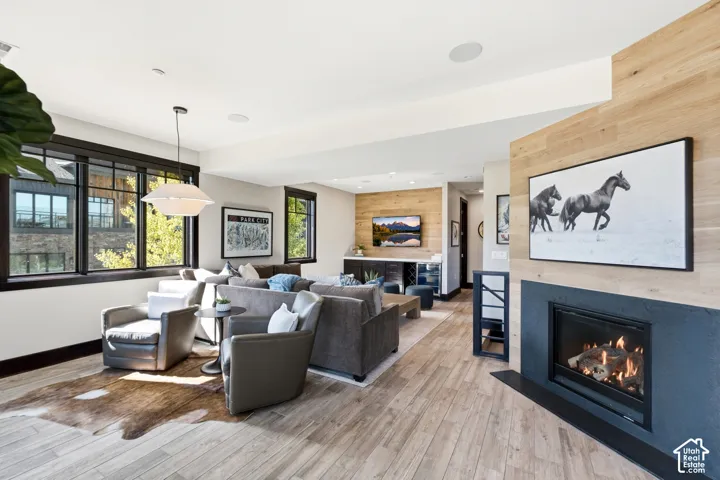 Fireplace featuring a matte black surround and wood-paneled accent wall, wood-finish flooring, built-in wet bar, and large multi-pane windows with dark frames