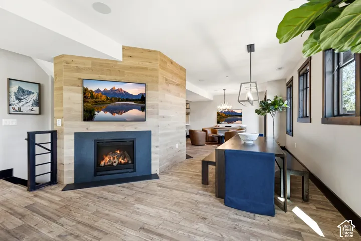Fireplace with dark stone surround and wood-plank accent wall, wood-finish flooring, and metal pendant lighting