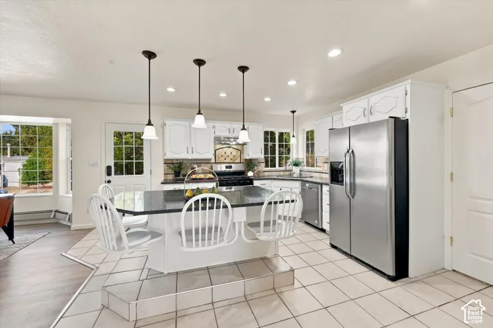 Kitchen featuring white cabinetry, a raised center island with stone-surface countertop, stainless steel refrigerator, recessed lighting, and tile flooring
