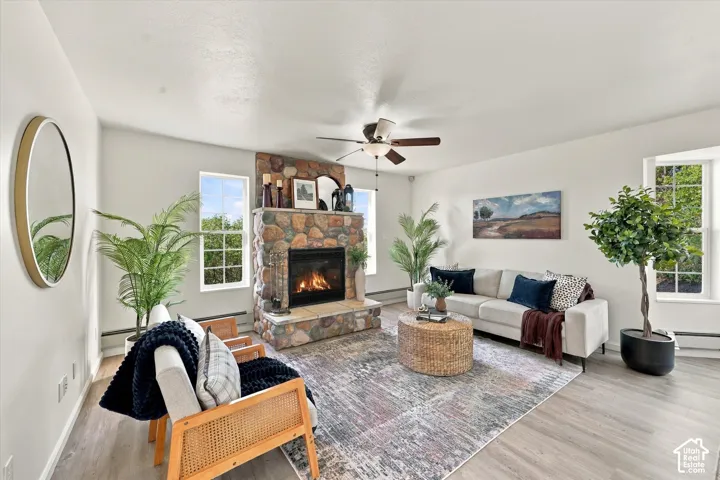 Living area featuring wood-finish flooring, a floor-to-ceiling stone fireplace with a raised hearth, multi-pane windows, and a ceiling fan