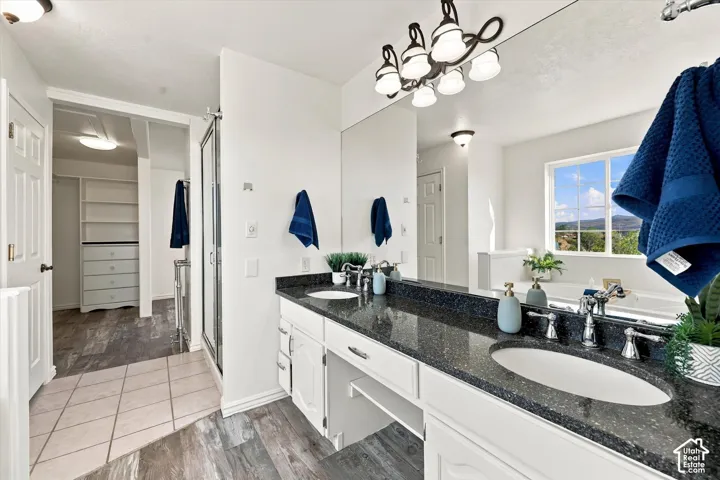 Primary Bathroom with Dual-sink vanity with dark stone countertop, full-width vanity mirror, multi-light fixture, glass-enclosed shower, and built-in shelving