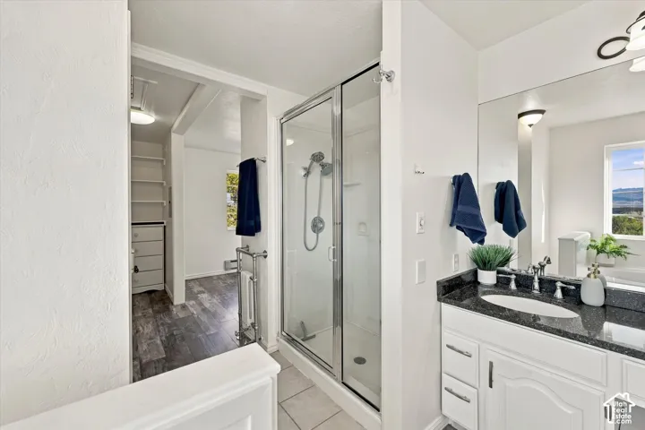 Primary Bathroom featuring a white vanity with dark stone countertop and oval under-mount sink, chrome-framed glass shower enclosure, and large wall-mounted mirror
