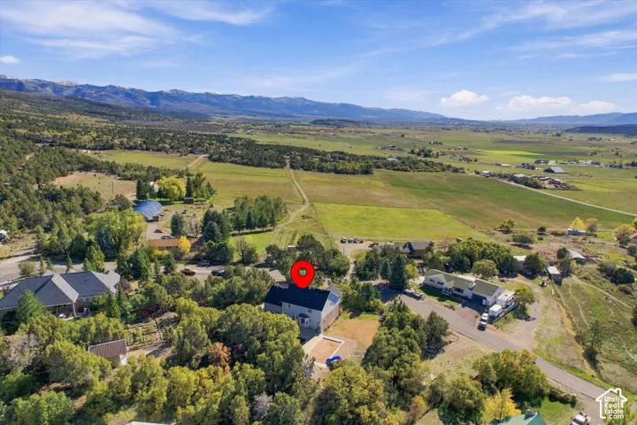 Aerial perspective featuring a multi-story residence with a pitched roof, an outdoor swimming pool, and extensive acreage set against a mountain backdrop