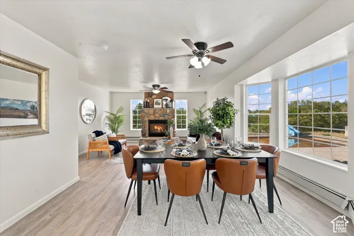 Open-concept interior featuring wood-finish flooring, full-height stone fireplace, multi-panel bay window, and dual ceiling fans