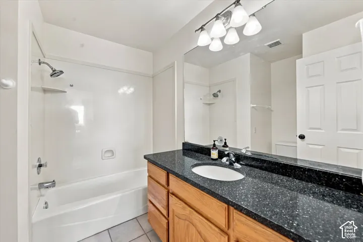 2nd Upstairs Bathroom featuring a dark stone-finish countertop with an integrated oval sink, wood-finish cabinetry, a large wall-mounted mirror, and a tub-shower combination with a surround