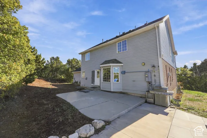Two-story exterior featuring light-colored horizontal siding, a brick facade accent, a ground-level concrete patio, and a multi-pane bay window