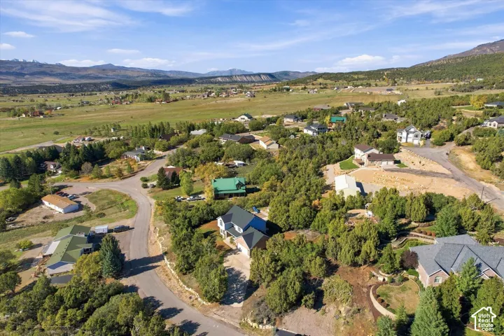 Aerial perspective featuring residential lots, mature trees, paved roadways, and mountain range scenery