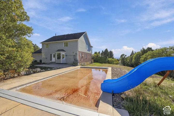 In-ground pool featuring a slide and concrete surround, paired with a multi-level residence with brick and siding exterior
