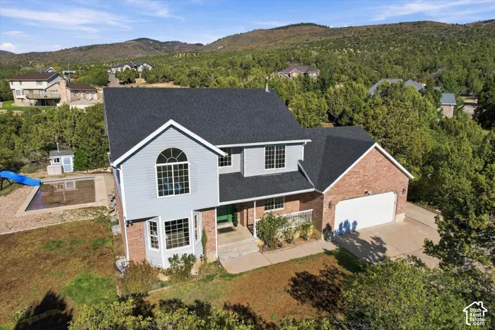 Two-story residence featuring a mixed brick and siding exterior, an attached two-car garage, an arched window element, and an in-ground pool, set against a mountainous landscape