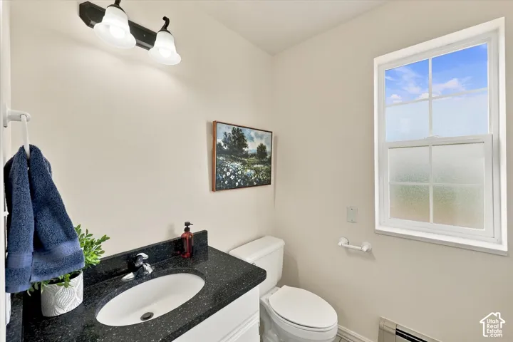 Main floor bathroom.  Vanity with a dark stone countertop, integrated oval sink, white cabinetry, two-light wall-mounted fixture, and a window with a muntin grid