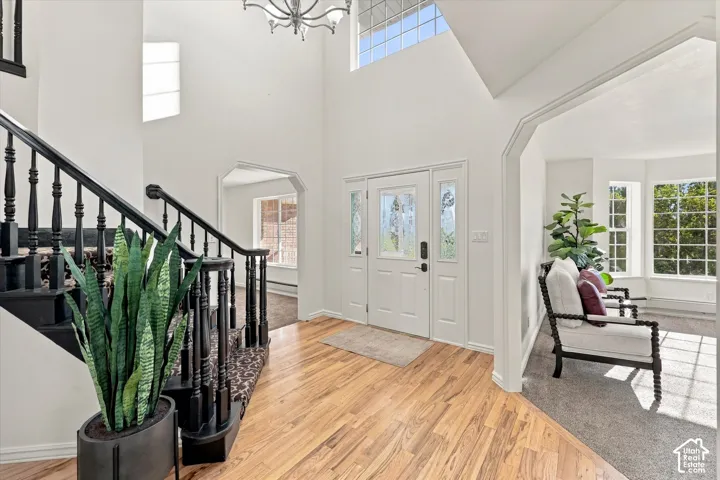 Entryway featuring a two-story ceiling, wood-finish flooring, a staircase with black railings, arched doorway openings, and a transom window