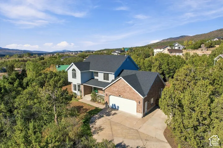 Two-story residence featuring a brick and siding exterior, asphalt shingle roof, attached two-car garage, and concrete driveway, set against a mountainous backdrop