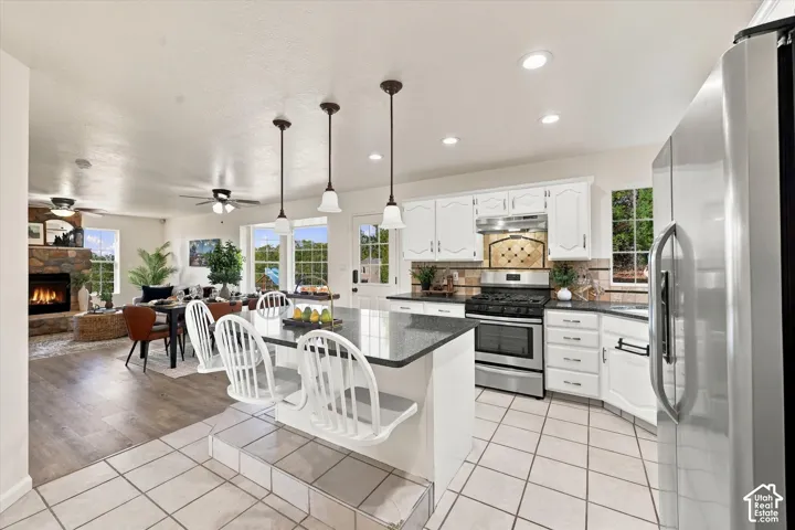 Kitchen featuring white cabinetry, a center island with countertop seating, stone-surround fireplace, stainless steel appliances, and tile flooring