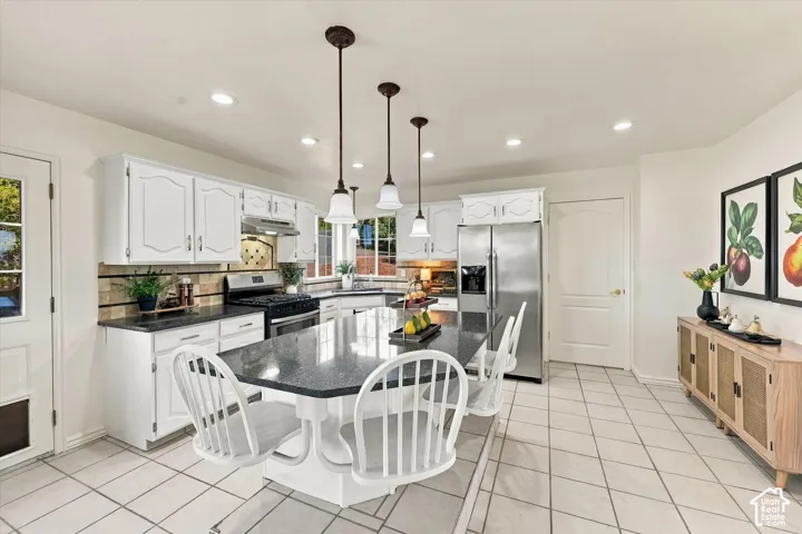 Kitchen featuring white cabinetry, stone-surface countertops, central island, stainless steel appliances, and tiled flooring