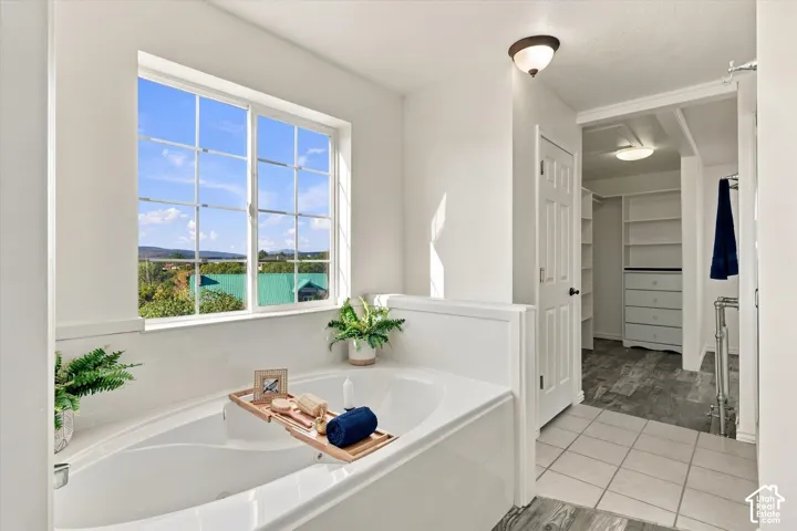 Primary Bathroom with soaking tub with a tile surround, large window with natural light, and walk-in dressing area featuring built-in shelving and tile flooring