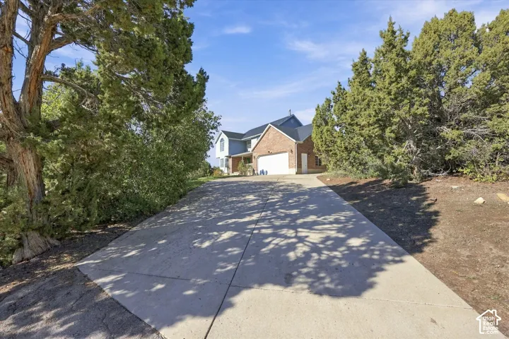 Brick and siding exterior featuring a concrete driveway, two-car garage, and mature juniper trees