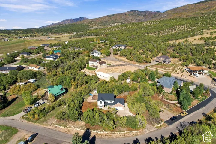Aerial perspective of a multi-level residential property featuring brick and siding exterior, attached garage, and mountain backdrop