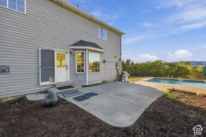 Exterior rear featuring light-colored horizontal siding, a concrete patio, a multi-pane bay window, and a private in-ground pool