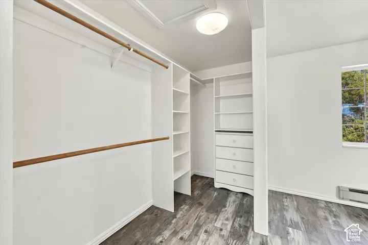 Walk-in closet featuring white built-in shelving, integrated dresser drawers, dual hanging rods, and wood-finish flooring