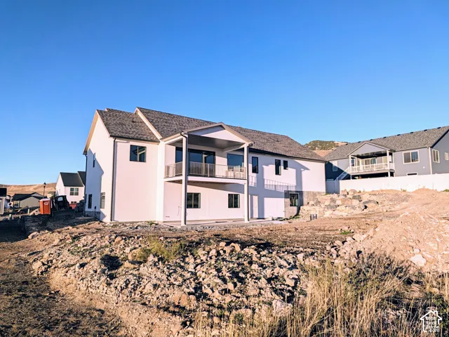 Two-story residence featuring light-toned siding, asphalt shingle roofing, an upper-level covered balcony with metal railing, and a ground-level concrete patio