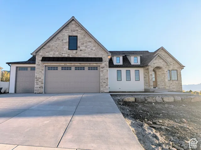 Stone and stucco exterior featuring a three-car garage, multi-gabled roofline, dormer windows, and a covered arched entryway