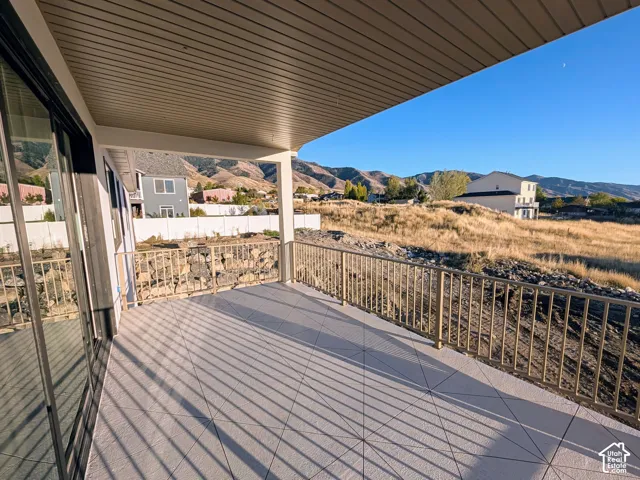 Covered patio featuring tiled flooring, metal railing, and sliding glass doors, accented by a mountainous landscape