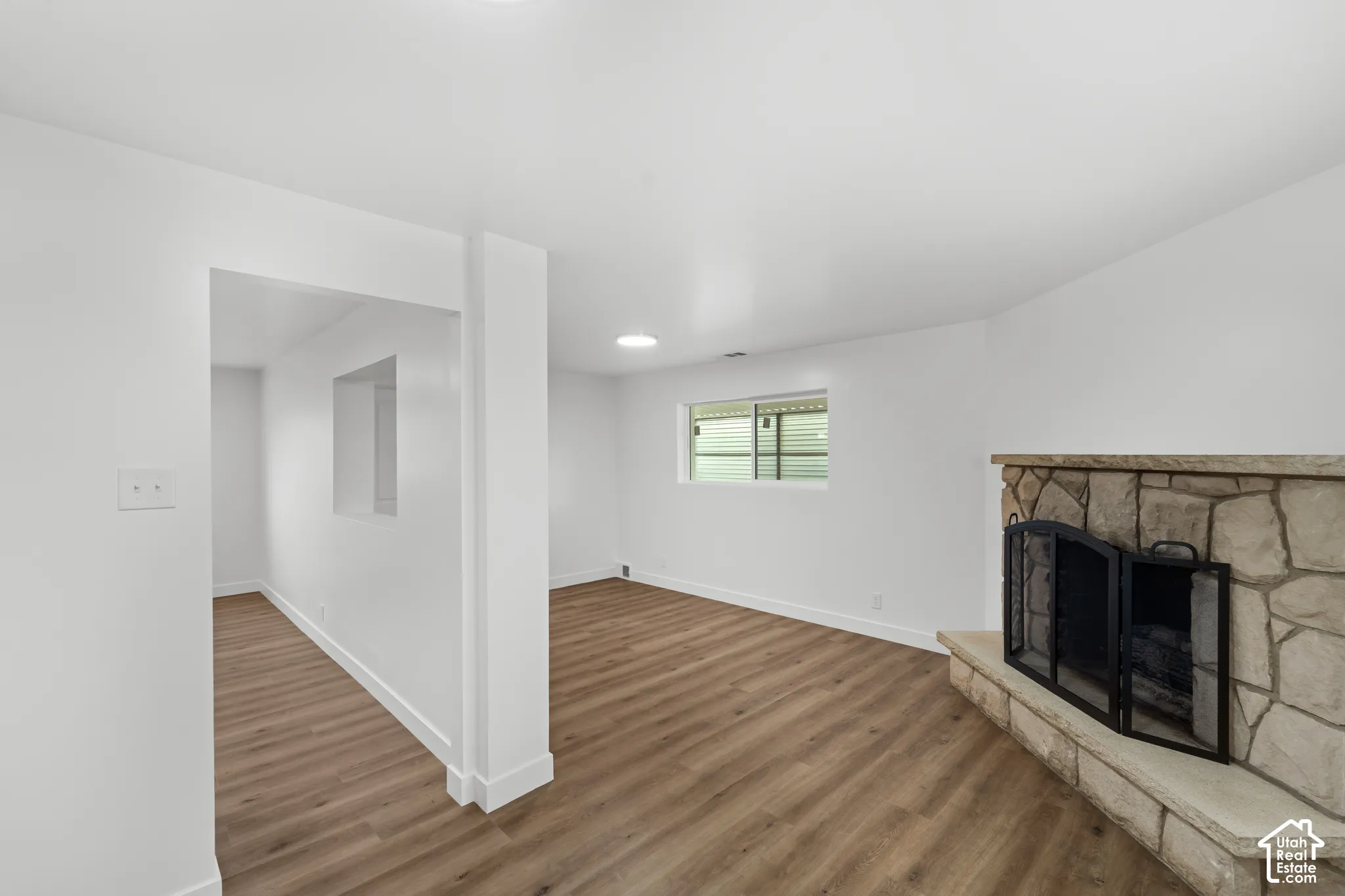 Interior space featuring wood-finish flooring, a stone-surround fireplace with a raised hearth, and a pass-through wall cutout