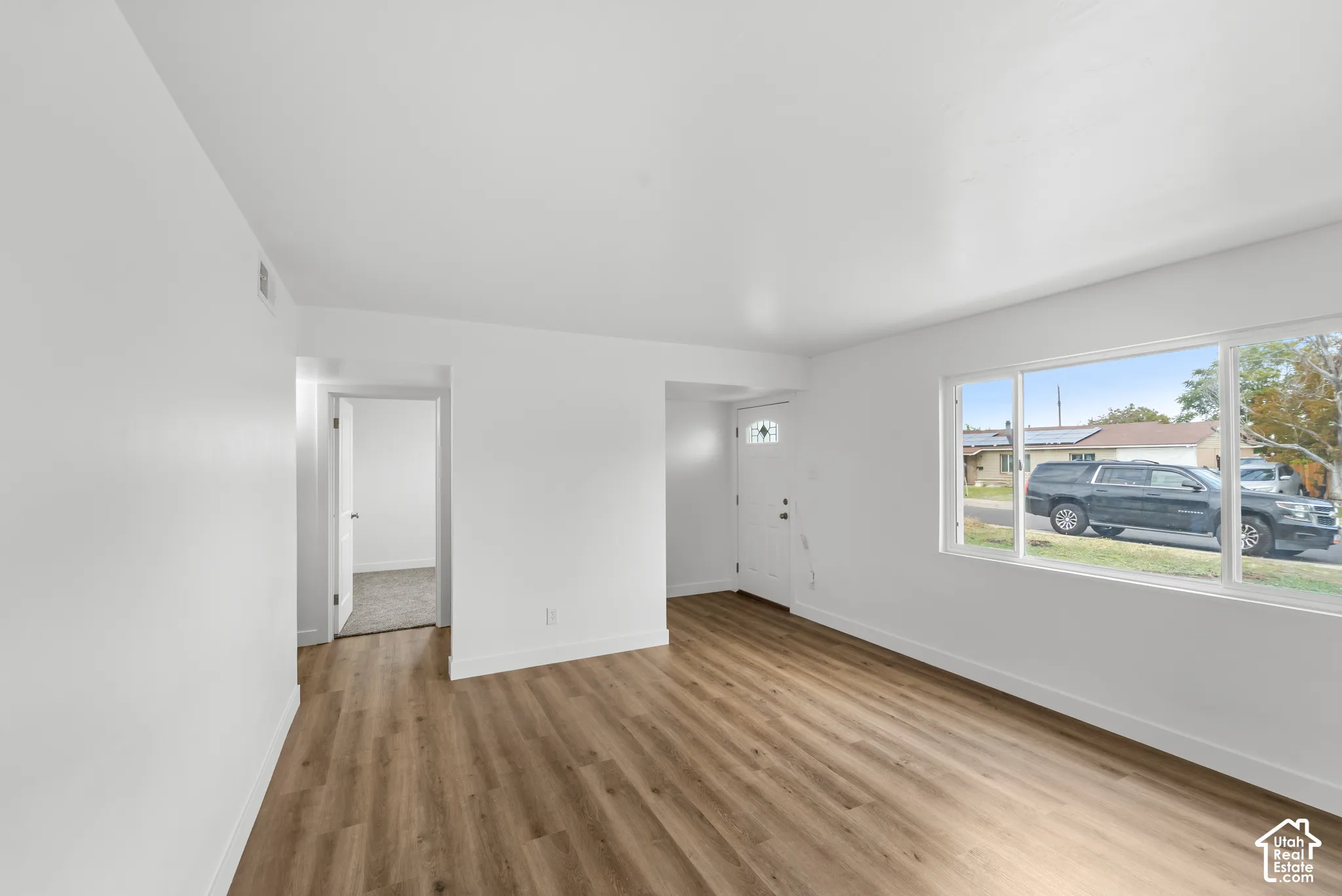 Interior space featuring wood-finish flooring, large window, neutral wall paint, and white paneled entry door with decorative glass insert