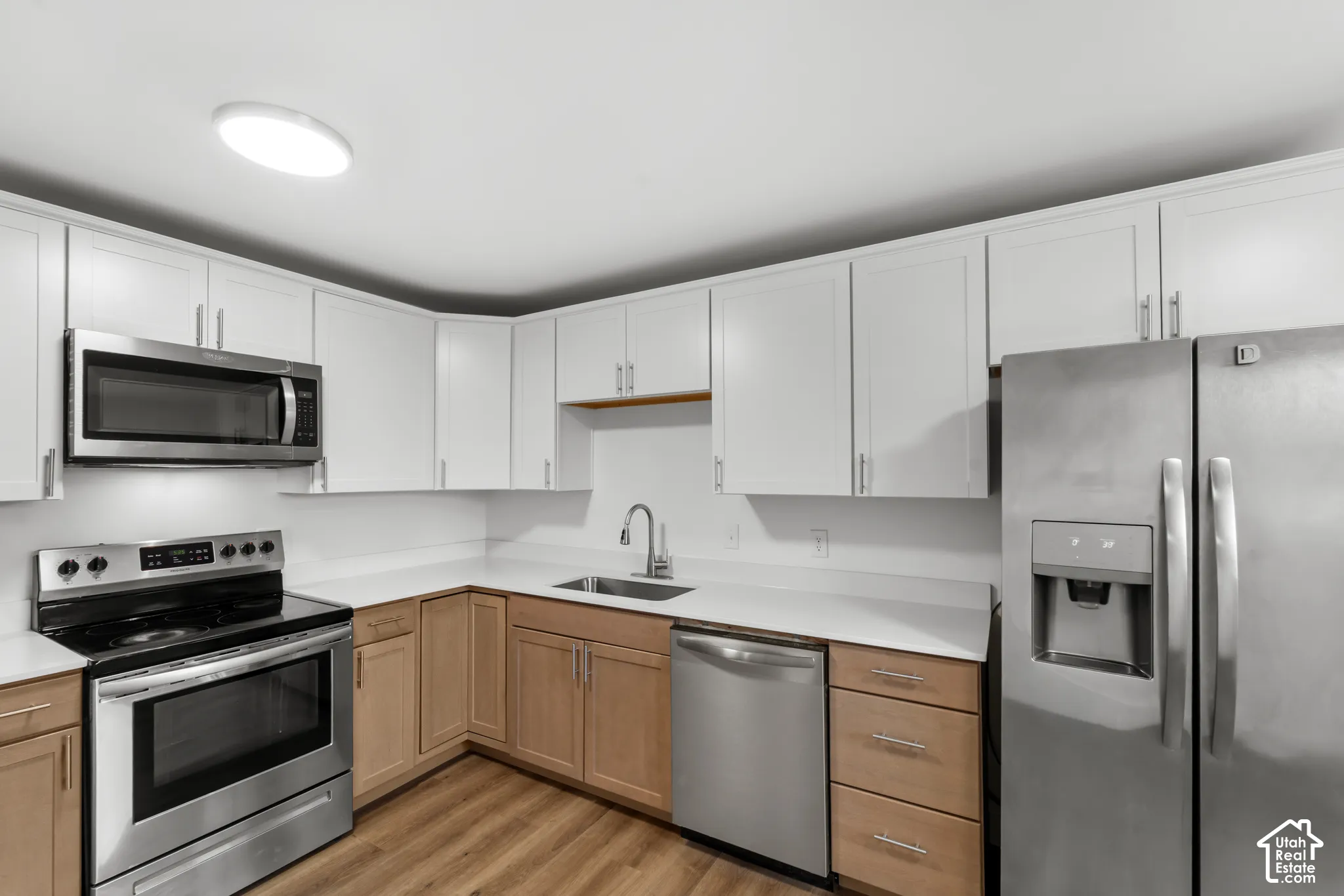 Kitchen featuring shaker-style cabinetry, solid-surface countertops, stainless steel appliances, a stainless steel undermount sink with a pull-down faucet, and wood-finish flooring