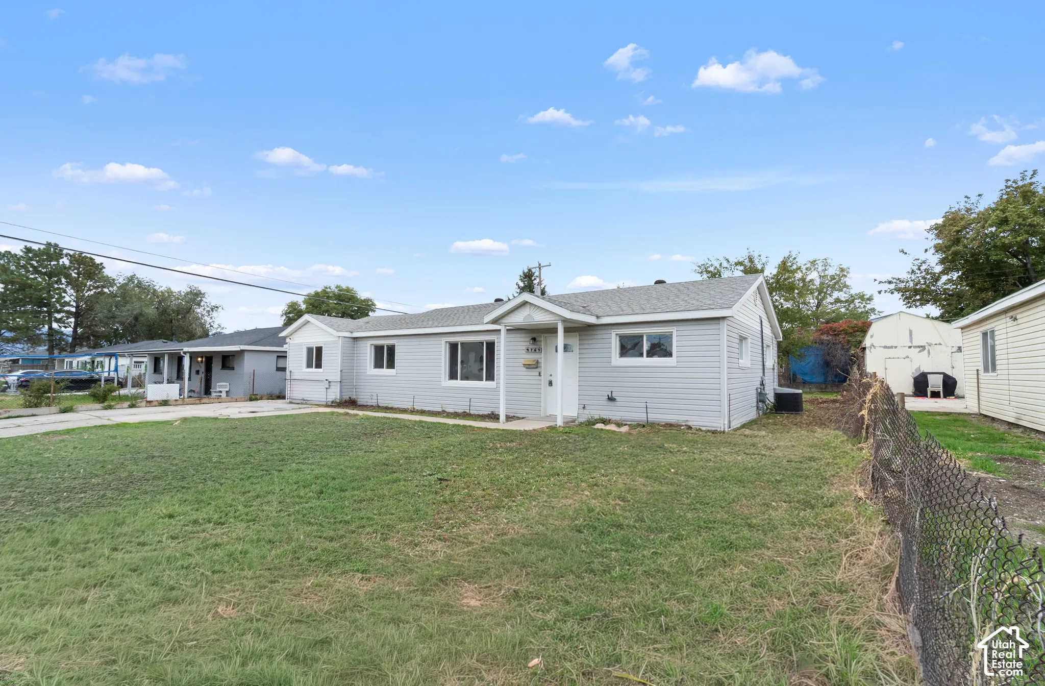 Single-story residence featuring light gray horizontal siding, a pitched roofline, a covered front entryway, and a chain-link fenced perimeter