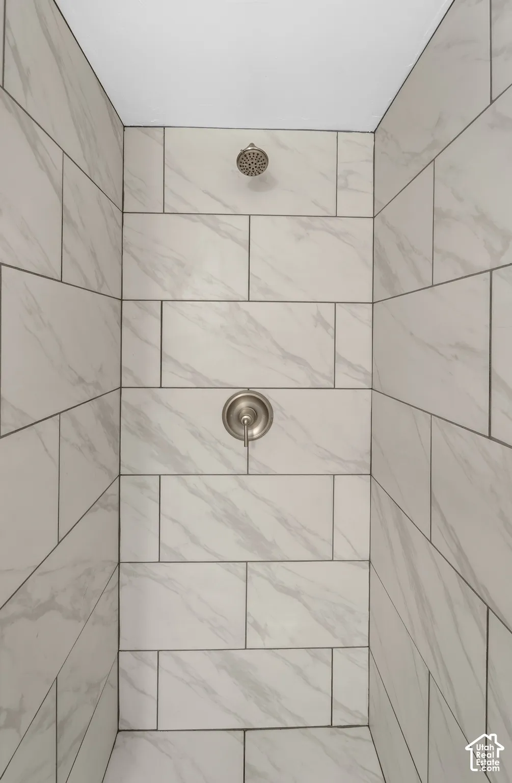 Shower enclosure featuring light-toned, large-format tile with decorative veining, offset pattern, and brushed-nickel hardware