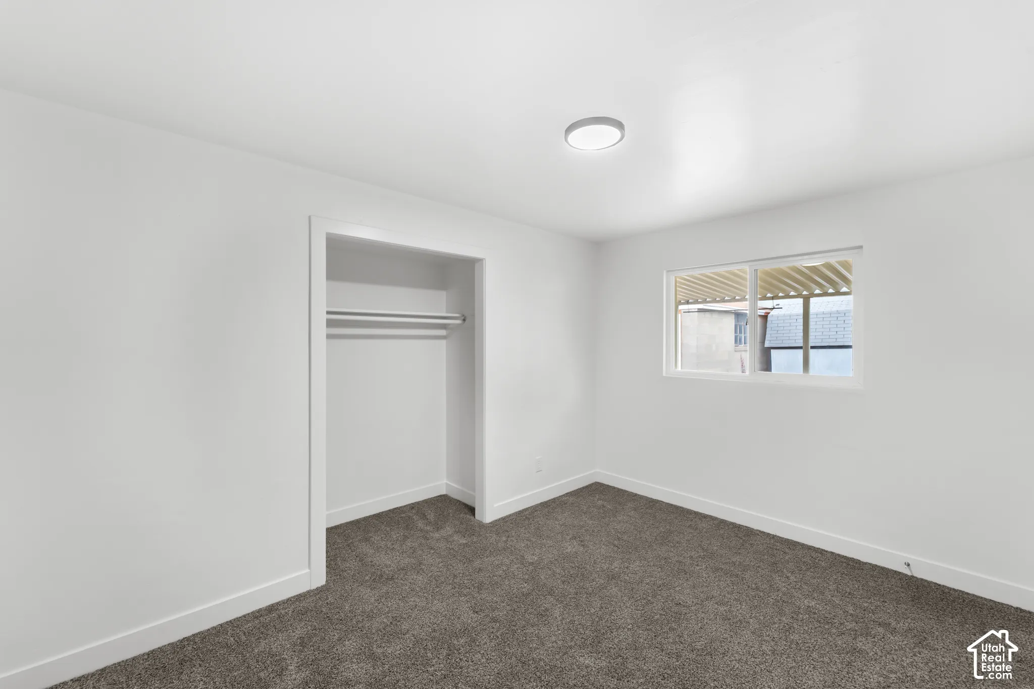 Interior space featuring neutral wall tones, gray carpeting, a sliding window with a built-in rod, and a recessed closet with a fixed hanging rod