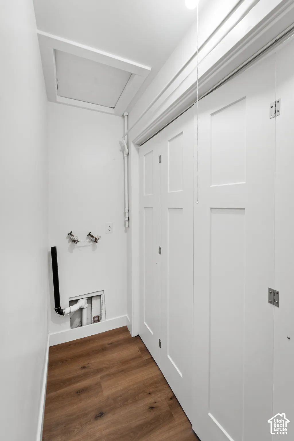 Wood-finish flooring, white shaker-style bi-fold closet doors, and recessed attic access panel