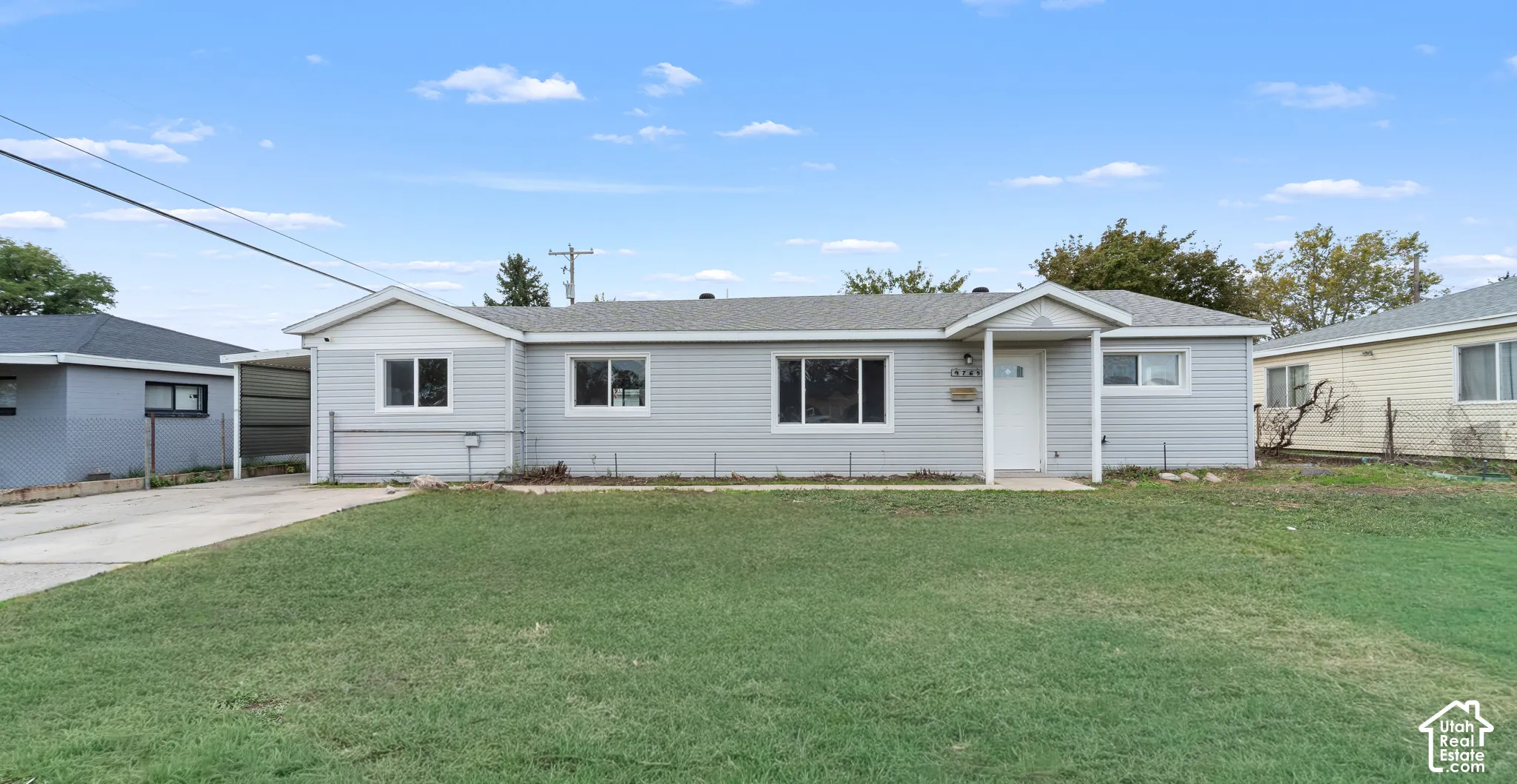 Single-story exterior featuring light-gray horizontal siding, a covered entryway, a concrete driveway, and an attached carport