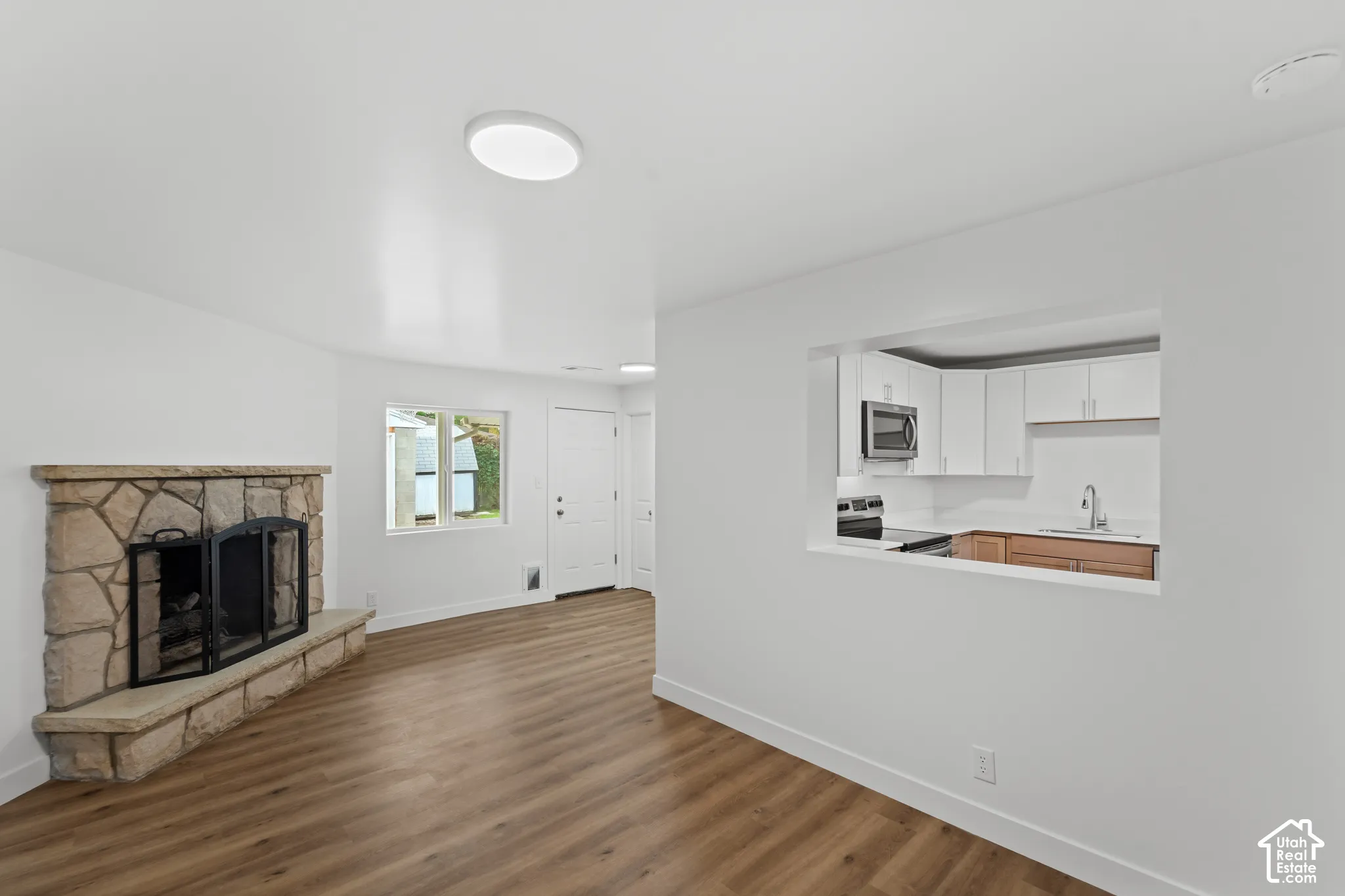 Stone-surround fireplace with a stone hearth, wood-finish flooring, and pass-through opening to the kitchen