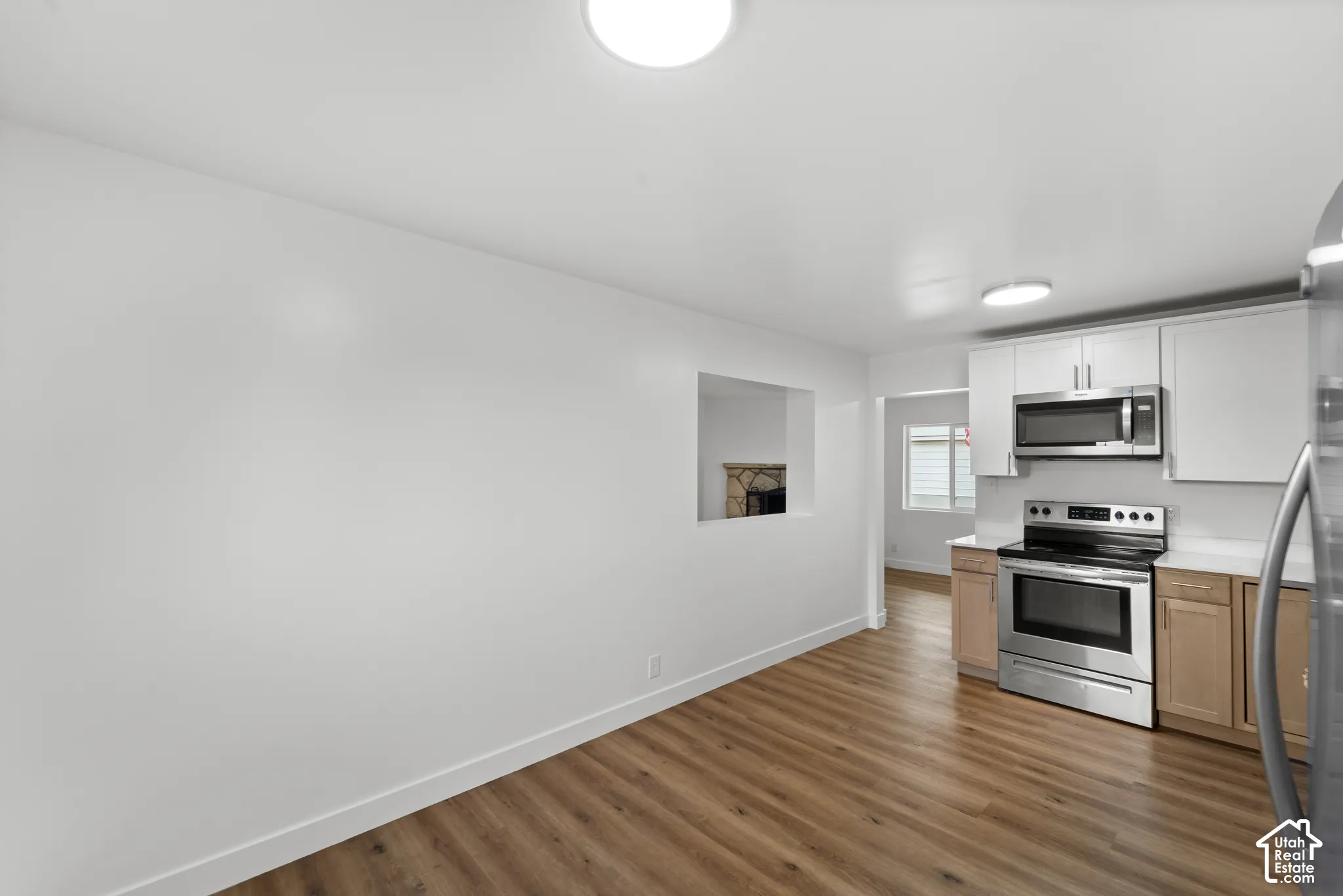 Kitchen featuring wood-finish flooring, stainless steel appliances, white upper cabinetry, and a pass-through opening