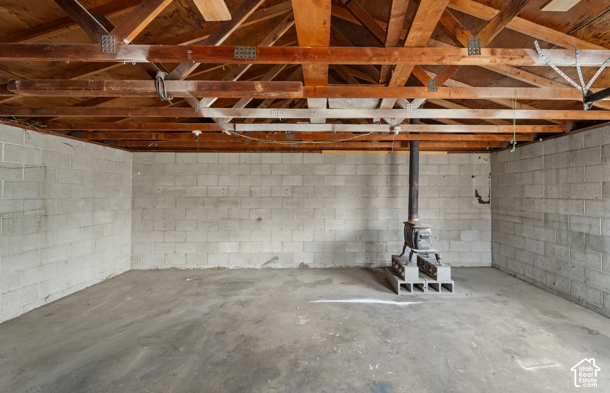 Open-concept workspace featuring exposed wood-truss ceiling rafters, concrete block wall construction, concrete flooring, and a free-standing metal stove