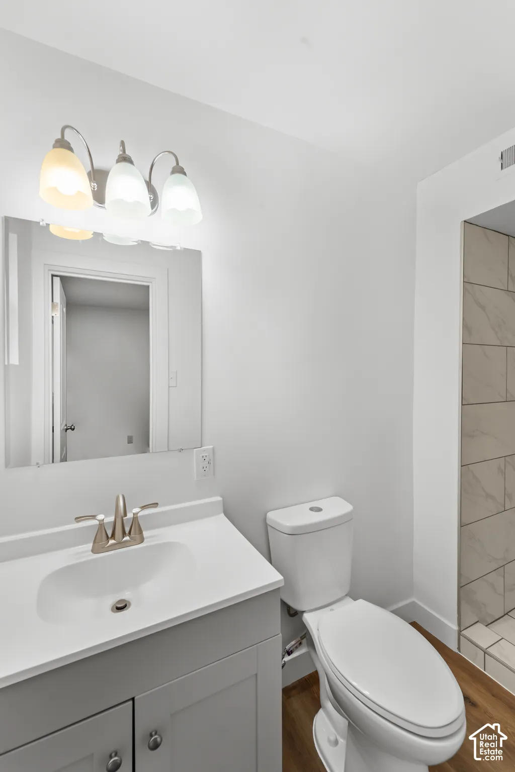Vanity with a solid-surface countertop and integrated sink, brushed nickel faucet, three-light fixture, mirror, and shower with neutral-toned wall tile