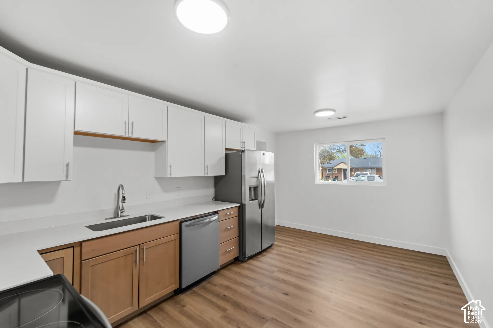 Kitchen featuring dual-tone cabinetry, white solid-surface countertops, stainless steel appliances, and wood-finish flooring