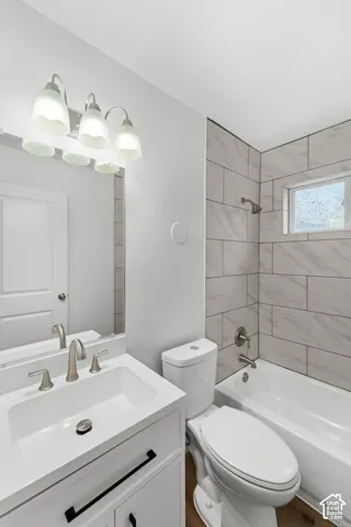 White vanity with an integrated countertop, three-light wall-mounted fixture, rectangular mirror, wood-finish flooring, and a tub-shower combination featuring horizontal stone-patterned wall tile