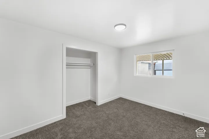 Interior space featuring neutral wall tones, gray carpeting, a sliding window with a built-in rod, and a recessed closet with a fixed hanging rod