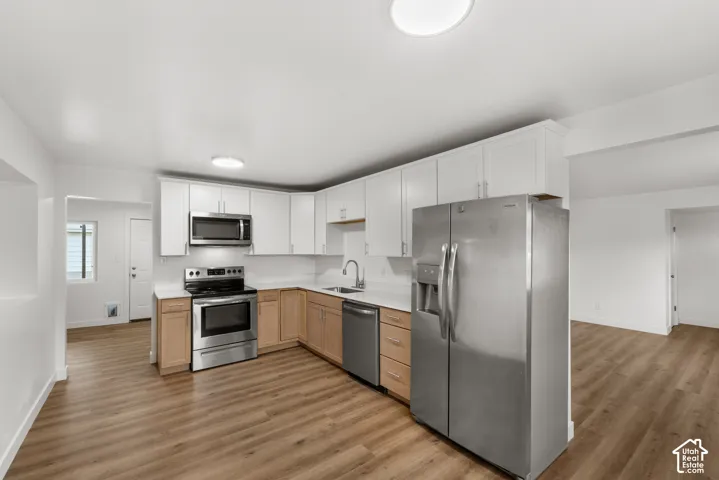 Kitchen featuring two-tone cabinetry, stainless steel appliances, solid-surface countertops, and wood-finish flooring