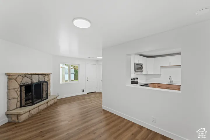 Stone-surround fireplace with a stone hearth, wood-finish flooring, and pass-through opening to the kitchen